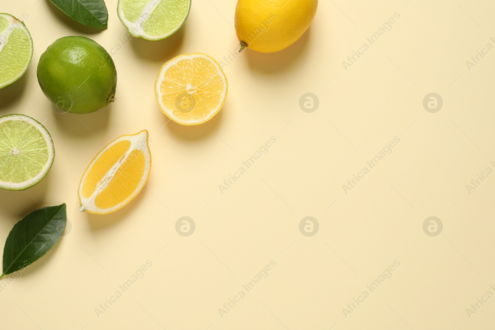 Photo of Fresh ripe lemons, limes and green leaves on beige background, flat lay. Space for text