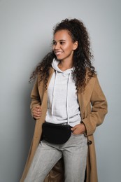 Beautiful African American woman with stylish waist bag on grey background