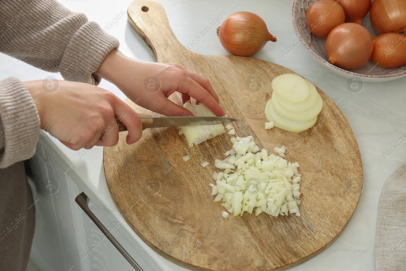 Photo of Woman chopping white onion on wooden board at table, closeup