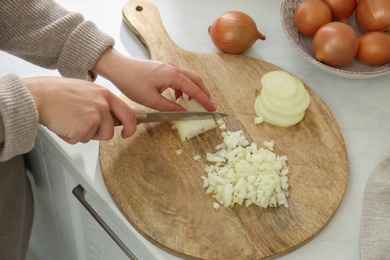 Photo of Woman chopping white onion on wooden board at table, closeup