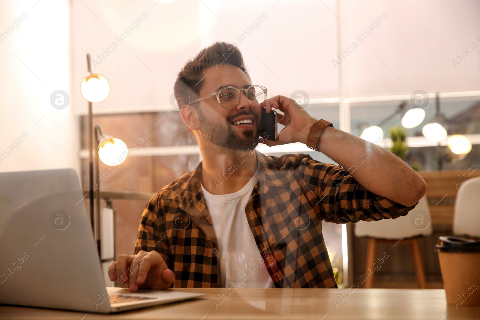 Photo of Man talking on smartphone while working with laptop in cafe