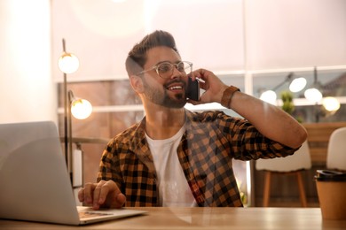 Man talking on smartphone while working with laptop in cafe