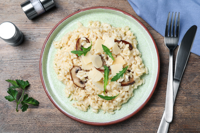 Photo of Delicious risotto with cheese and mushrooms on wooden table, flat lay