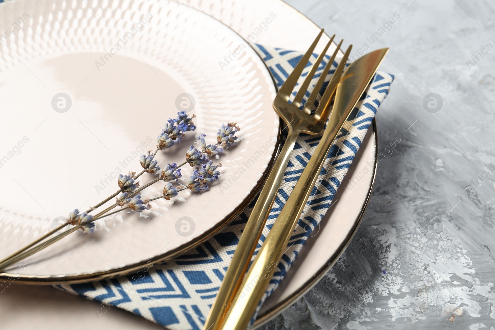 Photo of Clean plates, cutlery, napkin and lavender flowers on light grey textured table, closeup