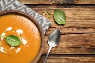 Photo of Tasty creamy pumpkin soup with basil in bowl on wooden table, flat lay. Space for text