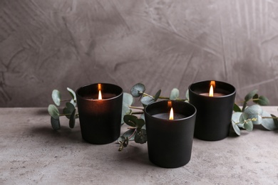 Burning candles and green branches on table