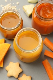 Jars with healthy baby food, pumpkin, carrot and cookies on grey background, above view