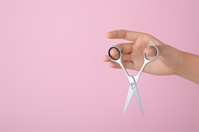 Photo of Hairdresser holding professional scissors and space for text on pink background, closeup. Haircut tool