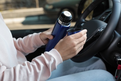 Woman with thermos on driver's seat of car, closeup 
