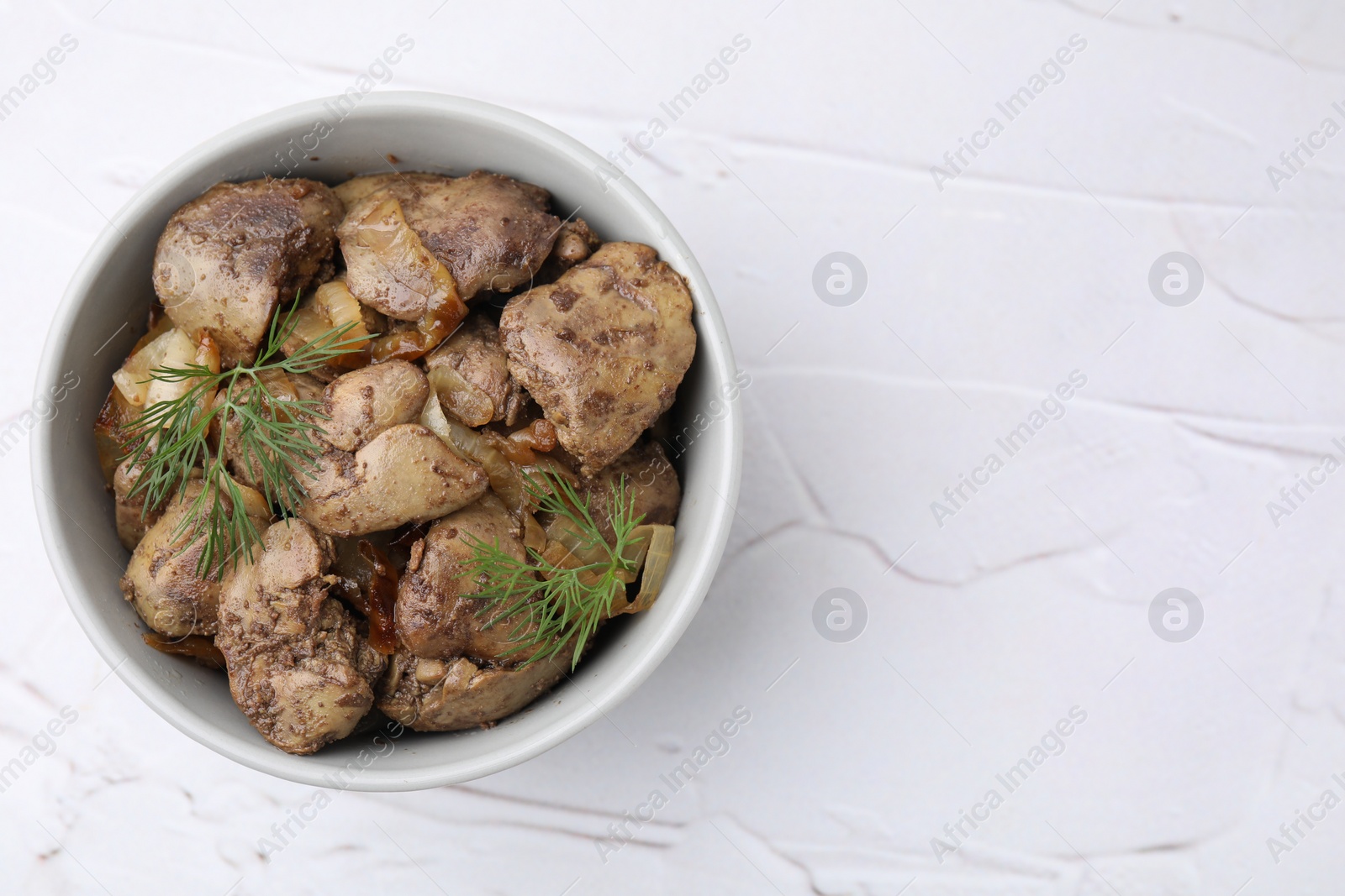 Photo of Tasty fried chicken liver with onion and dill in bowl on white textured table, top view. Space for text
