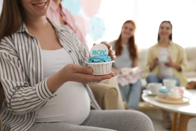 Photo of Pregnant woman with cupcake at home during baby shower party, closeup