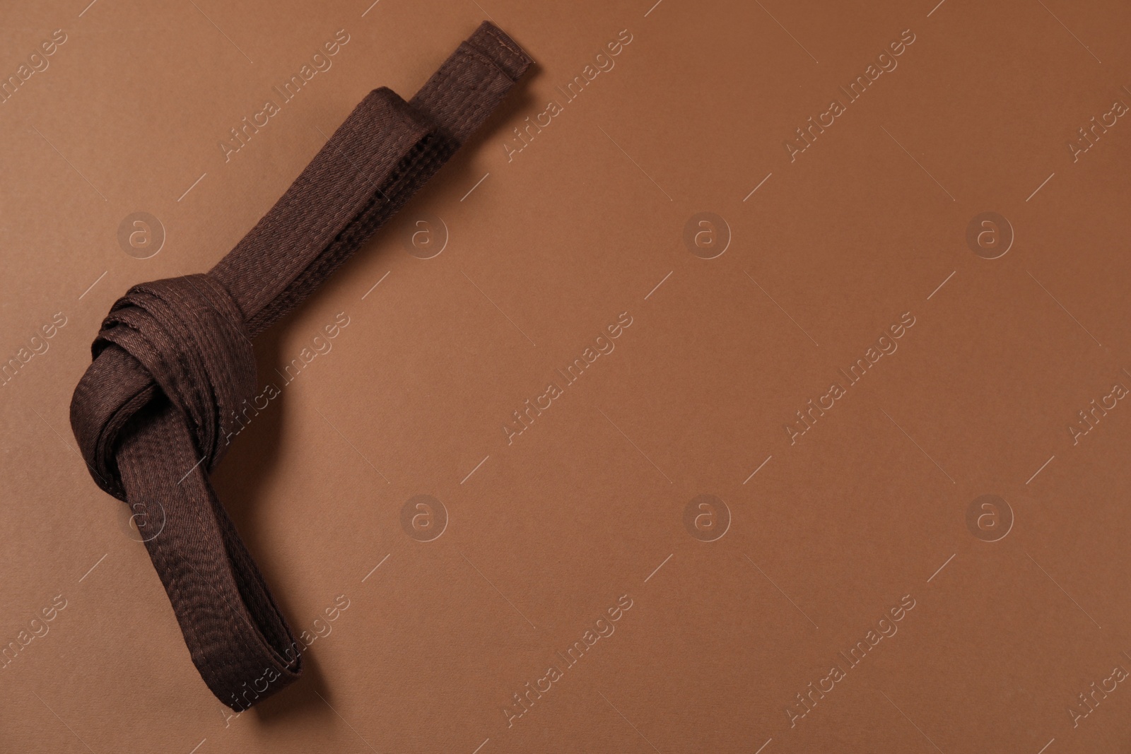 Photo of Karate belt on brown background, top view. Space for text