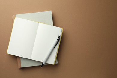 Photo of Notebooks and pen on light brown background, top view. Space for text