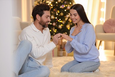 Making proposal. Man putting engagement ring on his girlfriend's finger at home on Christmas