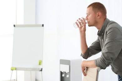 Man having break near water cooler at workplace. Space for text