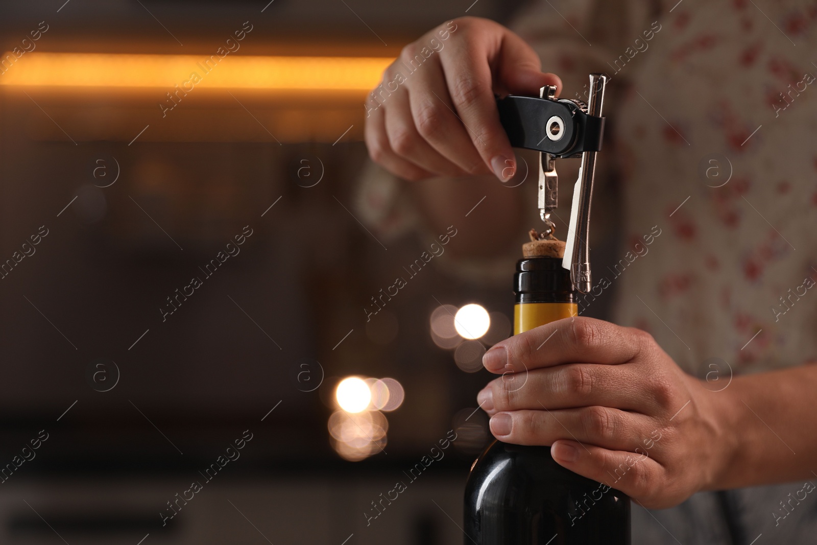 Photo of Woman opening wine bottle with corkscrew on blurred background, closeup. Space for text