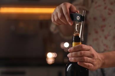 Woman opening wine bottle with corkscrew on blurred background, closeup. Space for text