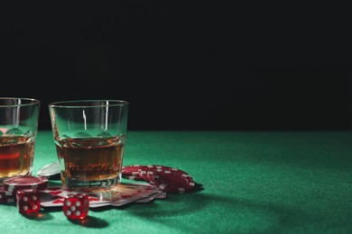 Photo of Casino chips, playing cards, dice and whiskey on green table, space for text