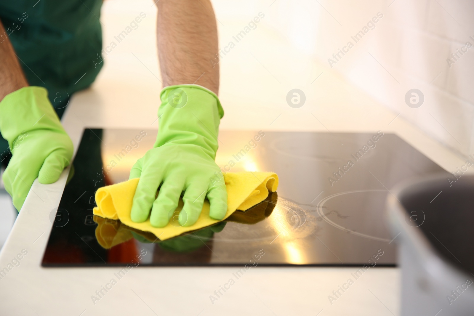 Photo of Professional young janitor cleaning stove in kitchen, closeup
