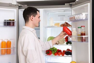 Photo of Happy man taking ketchup out of refrigerator in kitchen