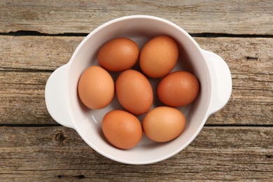 Unpeeled boiled eggs in saucepan on old wooden table, top view