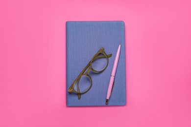 Blue office notebook, eyeglasses and pen on pink background, top view