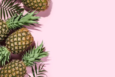 Whole ripe pineapples and green leaves on pale pink background, flat lay. Space for text