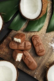 Photo of Delicious milk chocolate candy bars with coconut filling on black table, flat lay