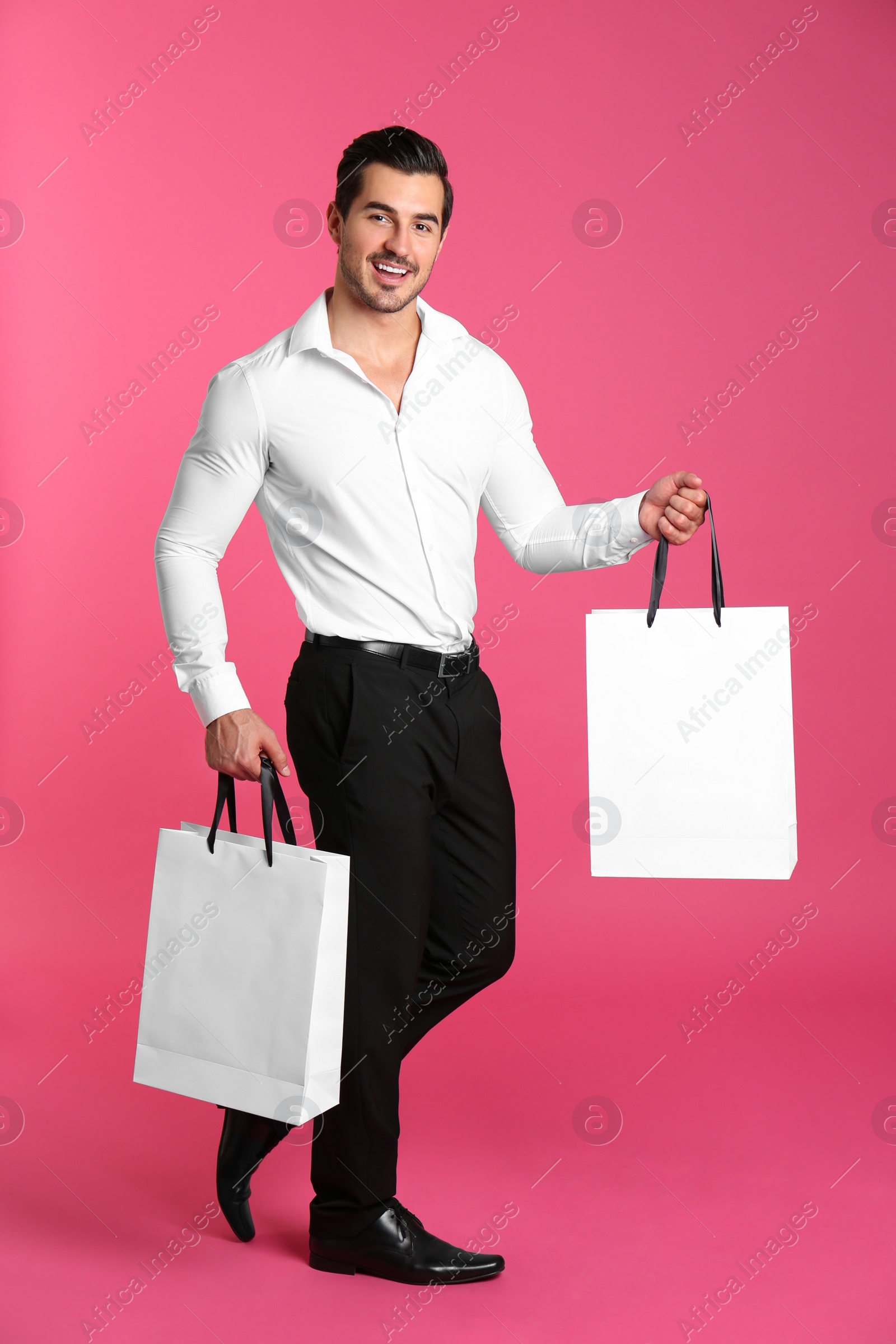 Photo of Young handsome man holding white paper bags on pink background. Mockup for design