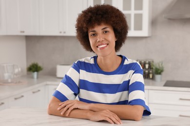 Photo of Happy young woman sitting at table in kitchen