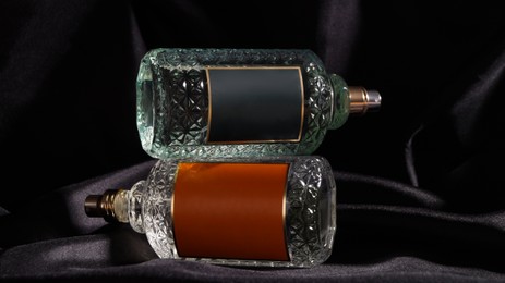 Photo of Luxury bottles of perfume on black silk, closeup