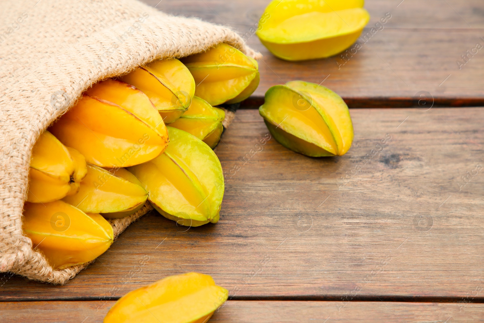 Photo of Sack with delicious ripe carambolas on wooden table