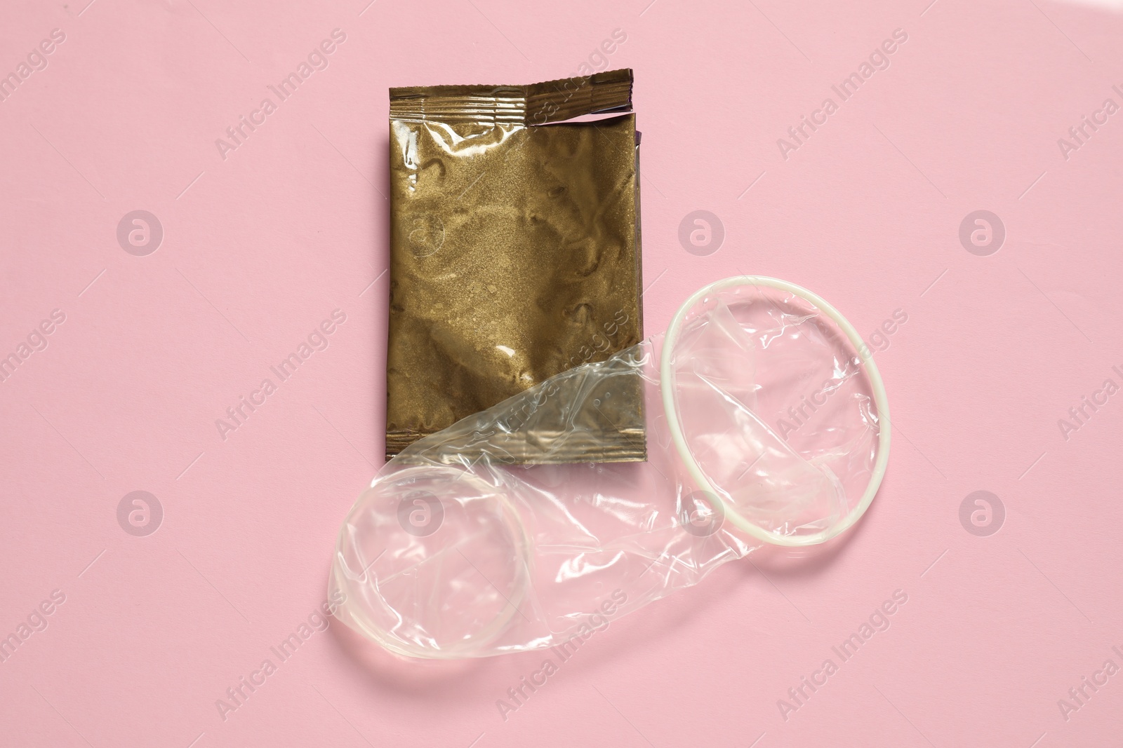 Photo of Unrolled female condom and torn package on light pink background, above view. Safe sex