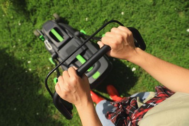Above view of woman cutting grass with lawn mower in garden on sunny day, closeup