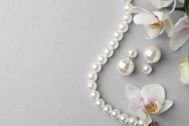 Photo of Elegant pearl earrings, bracelet and orchid flowers on white background, flat lay. Space for text