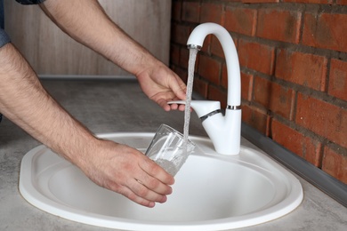 Man filling glass with water from faucet in kitchen, closeup