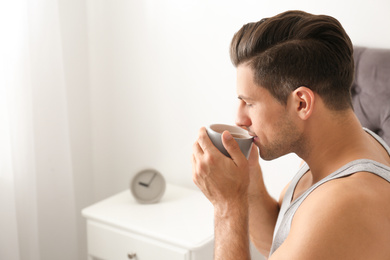 Man with cup of coffee in bedroom. Lazy morning