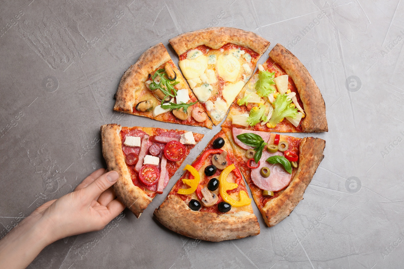 Photo of Woman taking slice of delicious pizza at grey table, top view