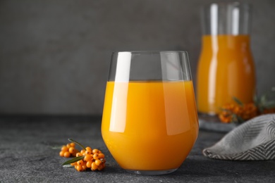 Delicious sea buckthorn juice and fresh berries on grey table, closeup