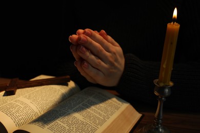 Photo of Woman praying at table with burning candle and Bible, closeup