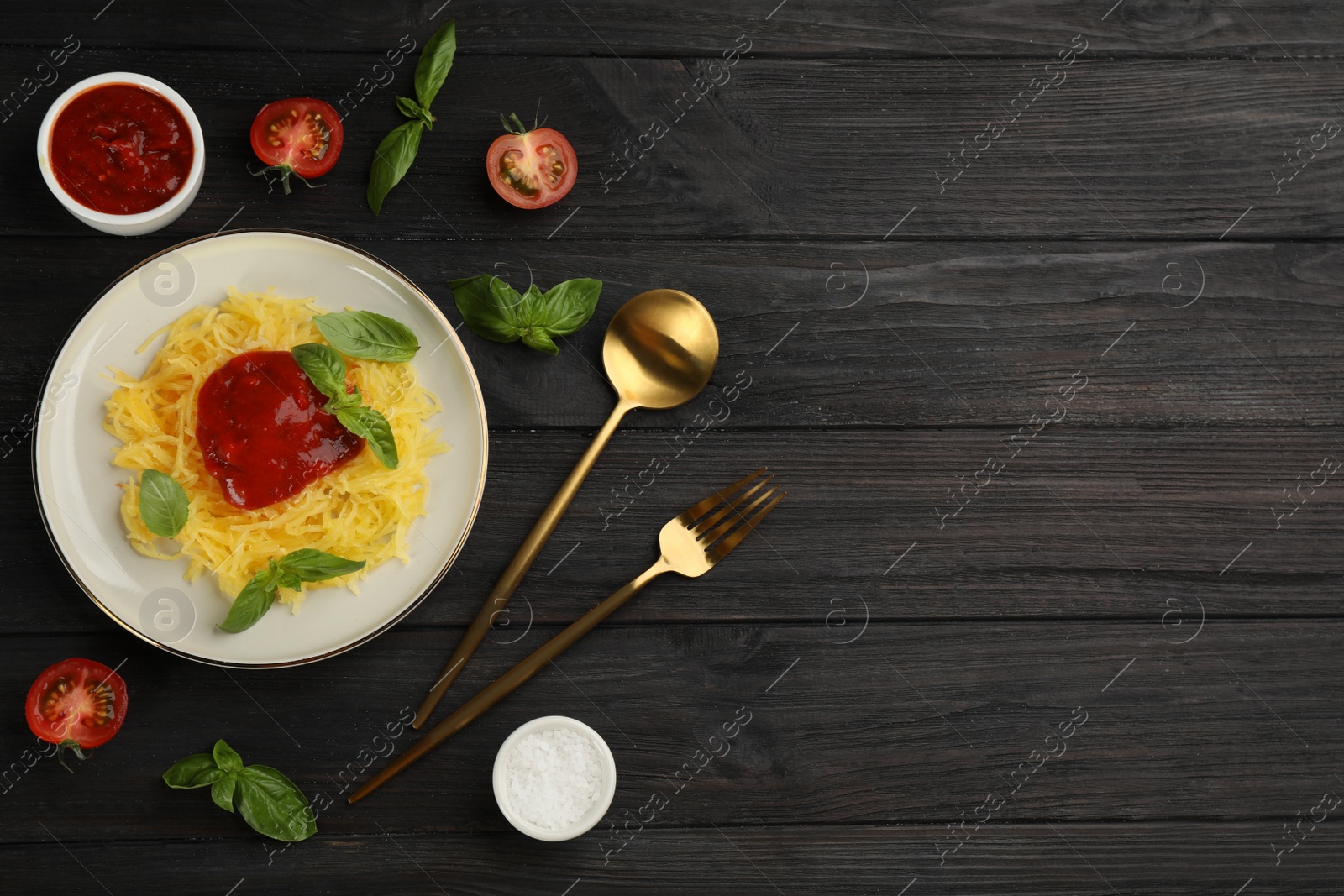 Photo of Tasty spaghetti squash with tomato sauce and basil served on black wooden table, flat lay. Space for text