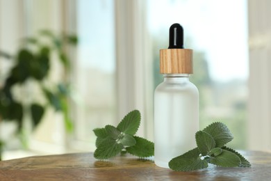 Bottle of mint essential oil and fresh herb on wooden table indoors, space for text