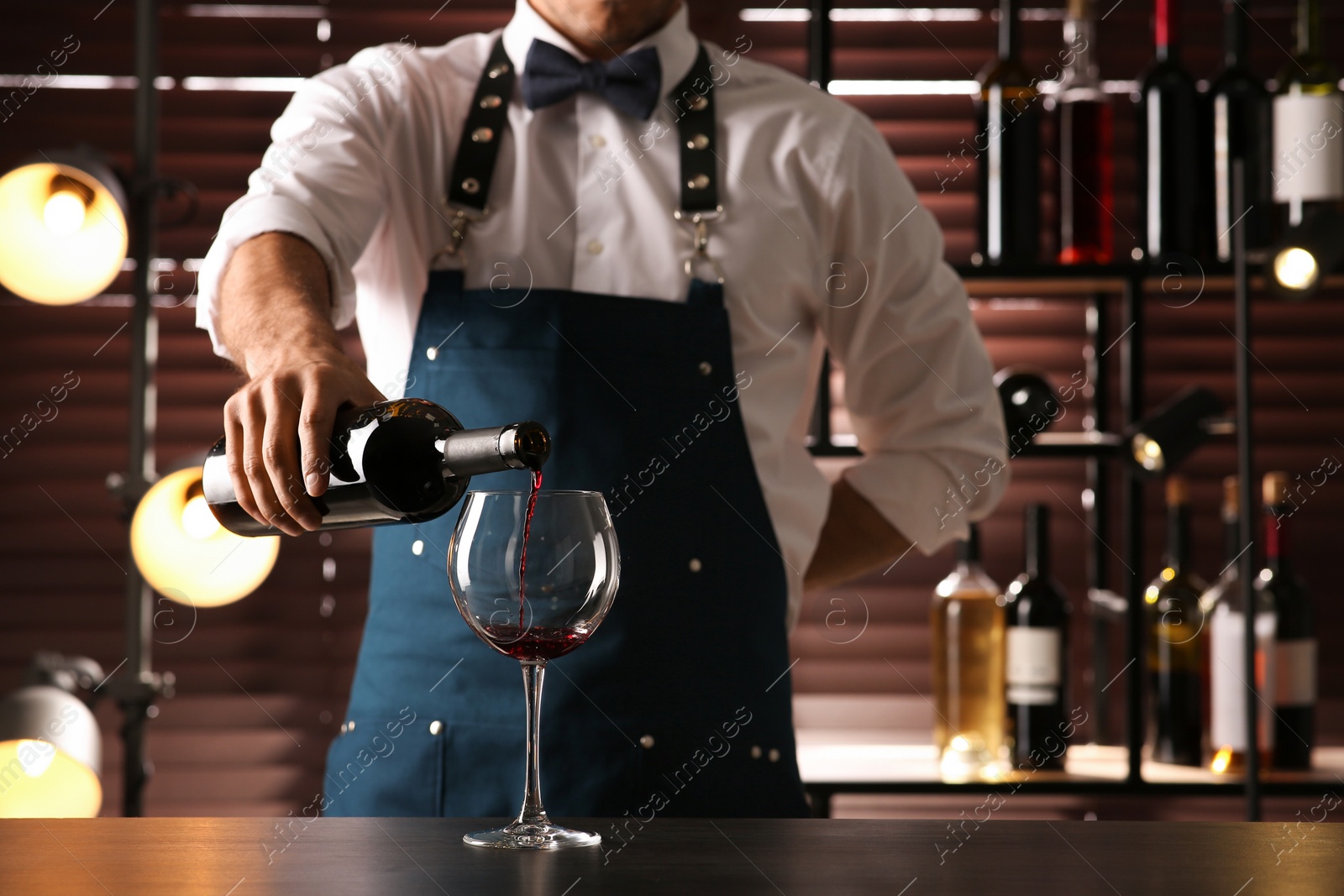 Photo of Bartender pouring red wine into glass at counter indoors, closeup