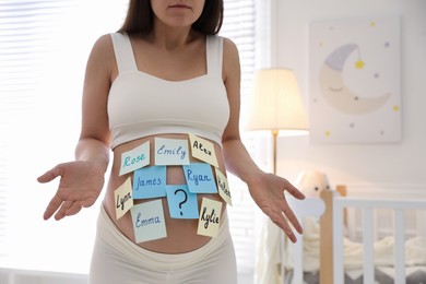 Photo of Pregnant woman with different baby names on belly at home, closeup