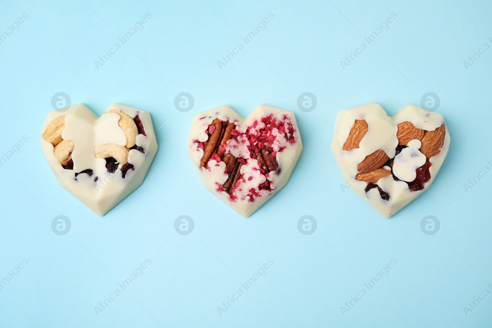 Photo of Tasty chocolate heart shaped candies with nuts on light blue background, flat lay