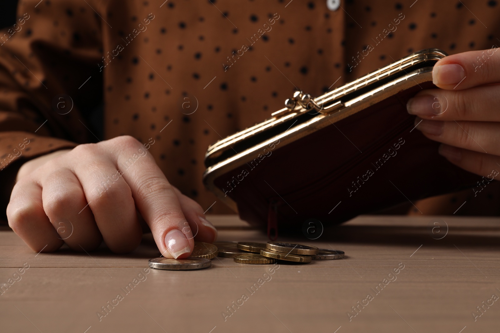 Photo of Poverty. Woman with wallet counting coins at wooden table, closeup