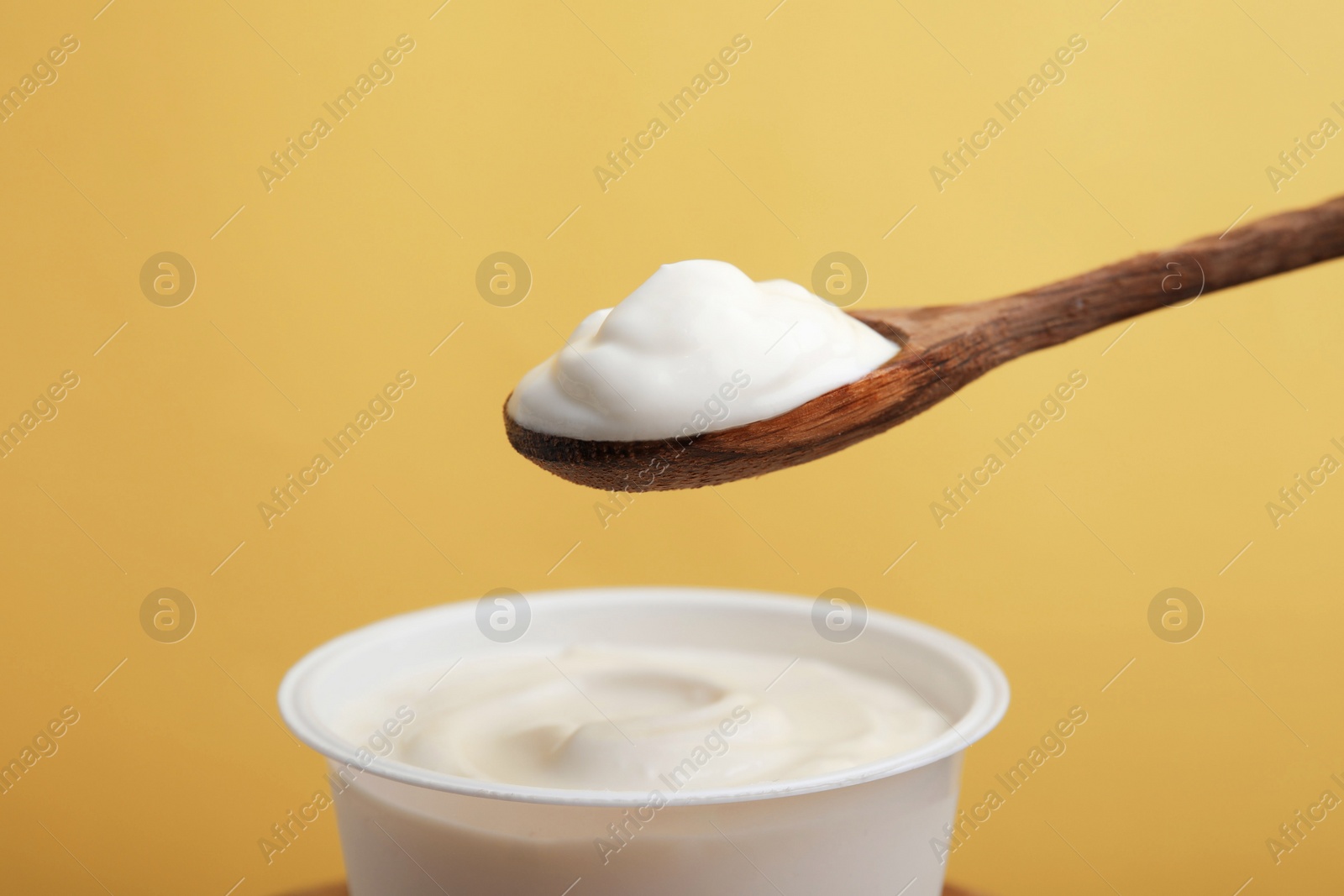 Photo of Eating delicious natural yogurt on yellow background