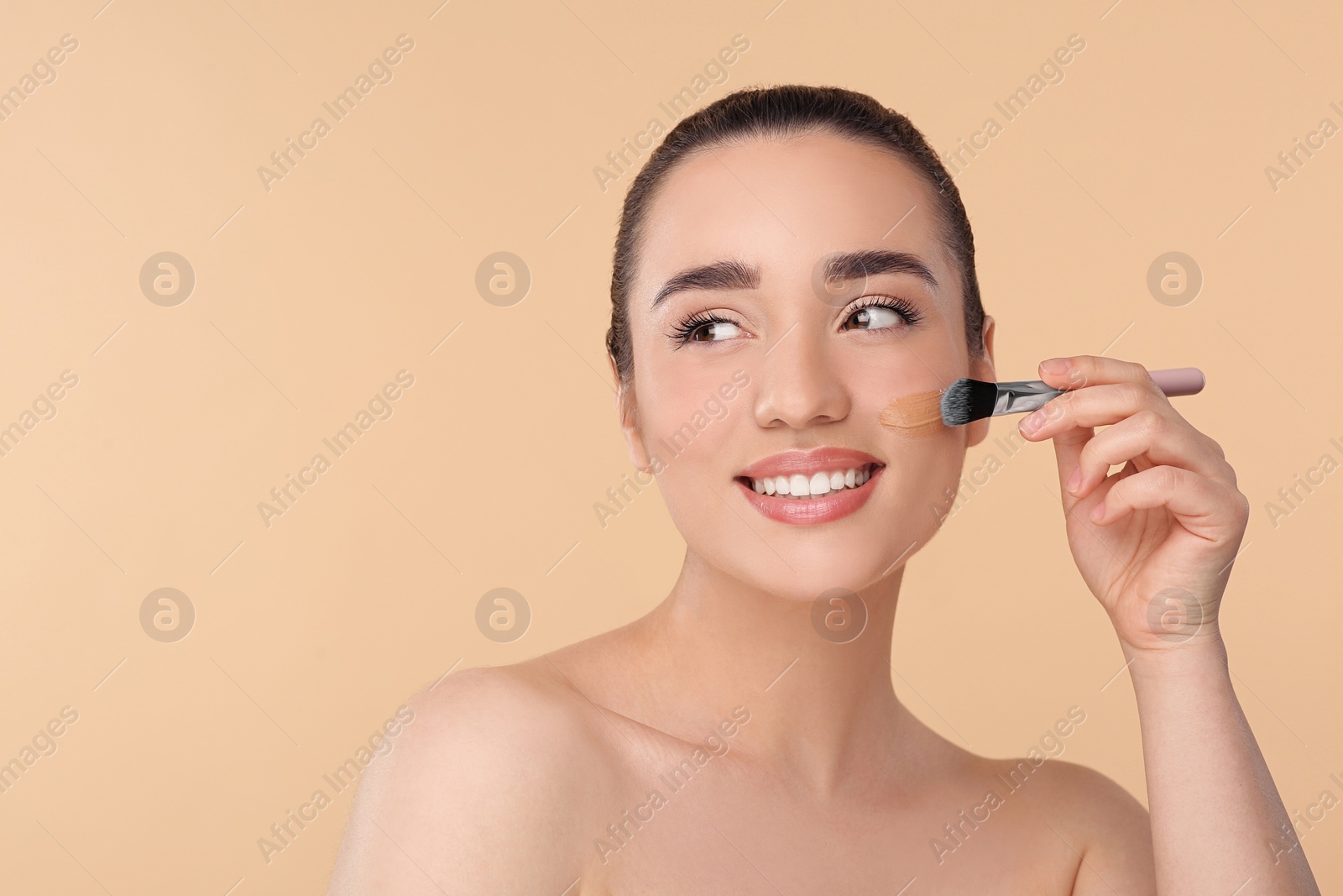 Photo of Woman applying foundation on face with brush against beige background