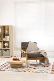 Stylish living room interior with comfortable armchair, blanket and side table