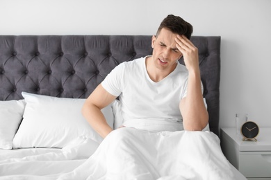 Photo of Young man with headache sitting in bed